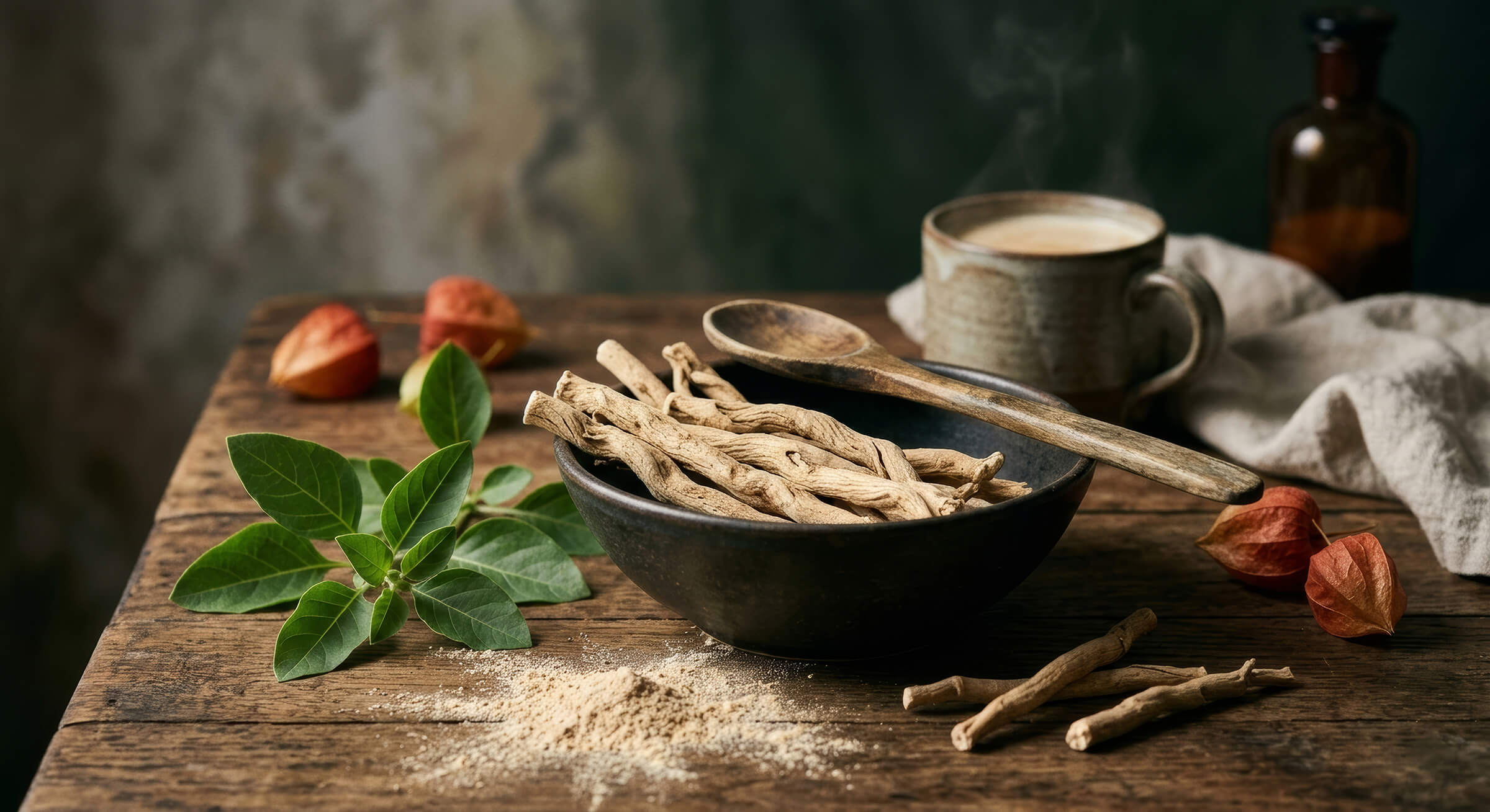 Dried ashwagandha roots and powder in a bowl with a wooden spoon and a cup of tea