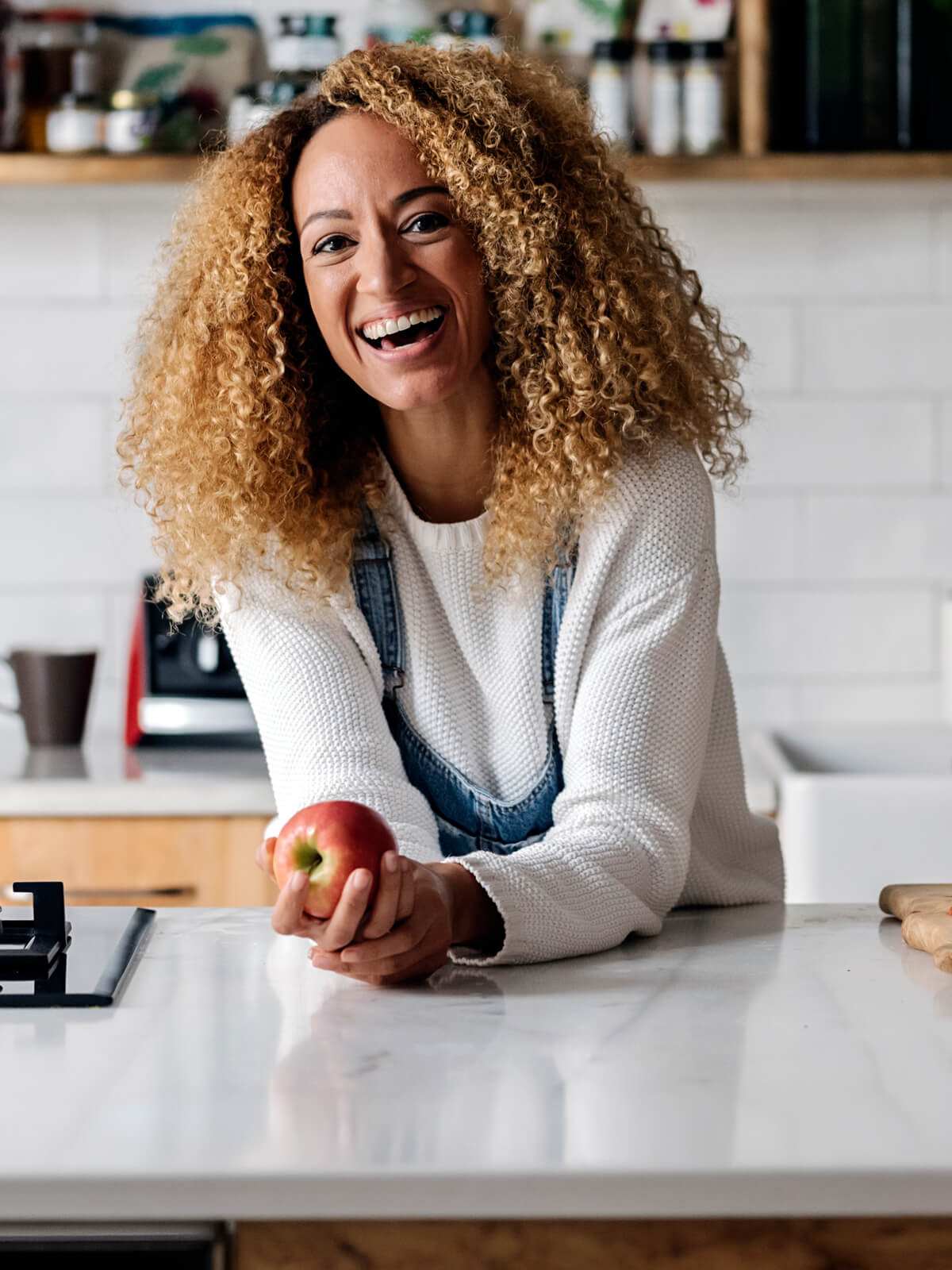 Smiling woman with curly hair leaning on her kitchen counter